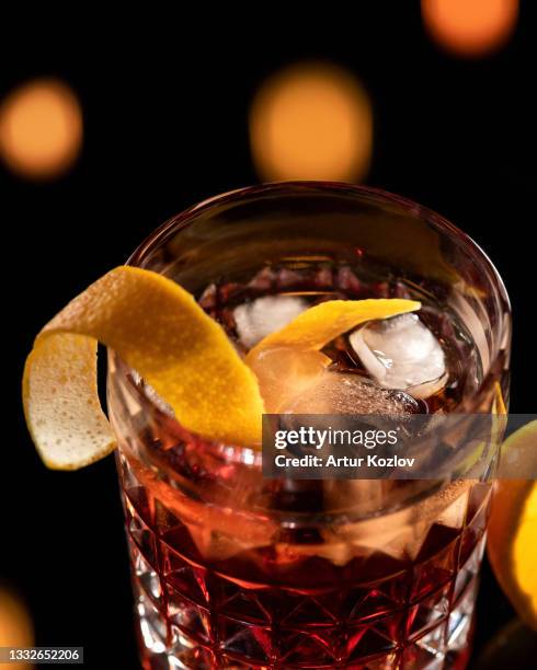 festive alcoholic drink. whiskey with orange zest and ice cubes in glass on blurred black background with bokeh. close-up shot. copy space. soft focus. vertical format - sabor - fotografias e filmes do acervo