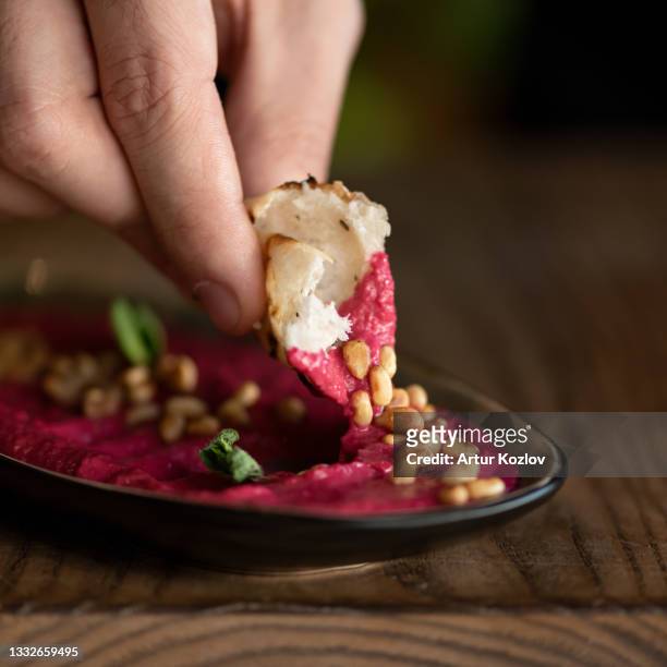 male hand dipping piece of pita bread into bowl with red hummus or dipping sauce. beetroot puree with peanuts, close-up shot. soft focus. copy space - dip stockfoto's en -beelden
