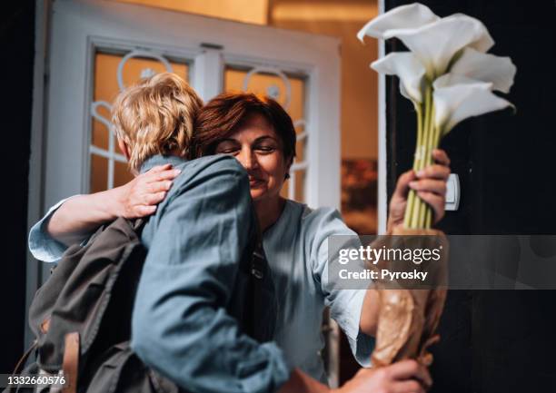 giovane che abbraccia una donna anziana alla porta - man giving flowers foto e immagini stock