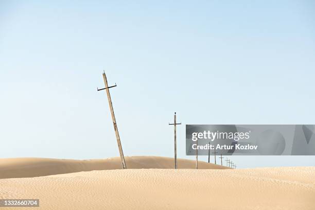 crosses line in sand desert. christian symbol of faith and hope. old cross-shaped pillars on sky background. ancient power electrical transmission. copy space - religiöses symbol stock-fotos und bilder