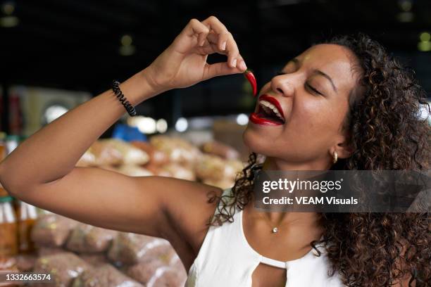 young african woman with curly hair wearing a white dress eating chili in a marketplace. - chili woman ストックフォトと画像