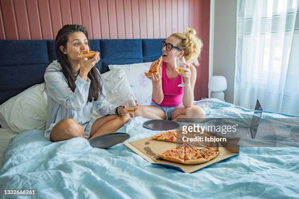 female friends eating pizza on the bed - avond thuis stockfoto's en -beelden