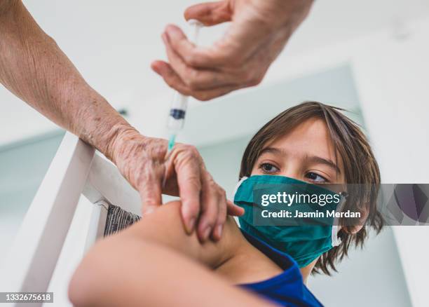 child wearing mask getting vaccinated by doctor holding a needle - 三種混合予防接種 ストックフォトと画像