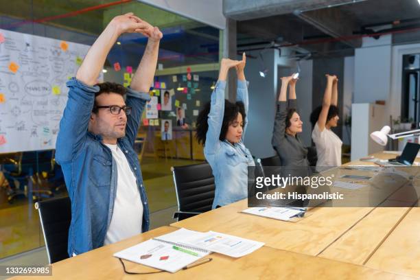 workers doing stretching exercises in a business meeting at the office - werken stockfoto's en -beelden