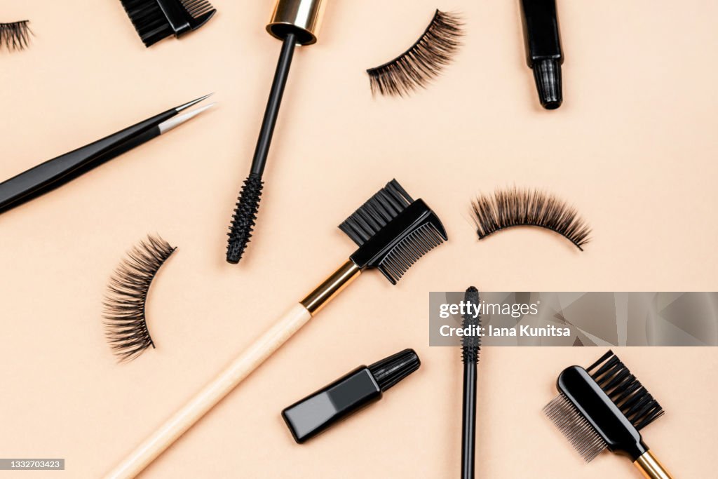 Various tools for eye lash extensions on trendy pastel beige background. Makeup accessories. Cosmetics. Fake eyelashes, glue, brush and tweezers.