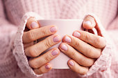 Cup of coffee or tea in woman's hands with soft pink manicure