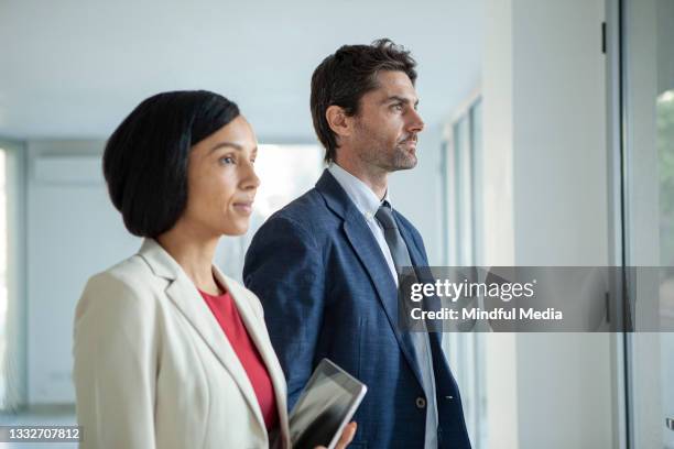 confident latin businessman and businesswoman looking through window - corporate media modern bright stockfoto's en -beelden