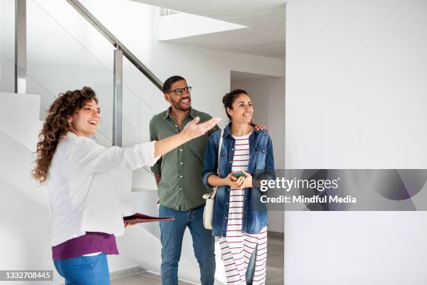 real estate agent showing new apartment to happy young latin couple - house showing stock pictures, royalty-free photos & images