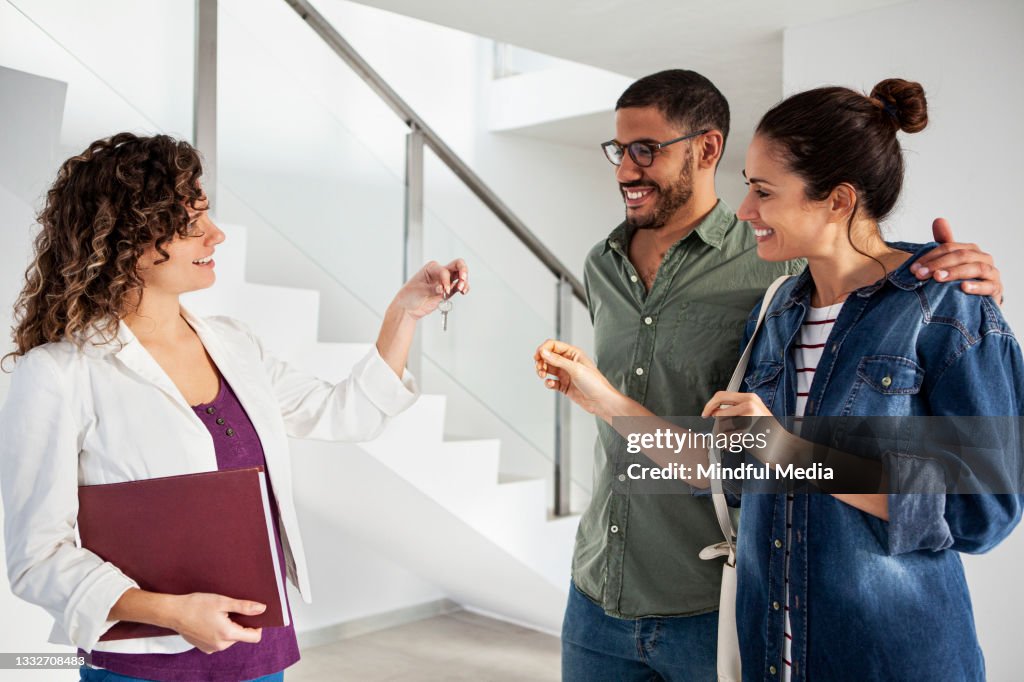 Young latin couple receiving keys from real estate agent