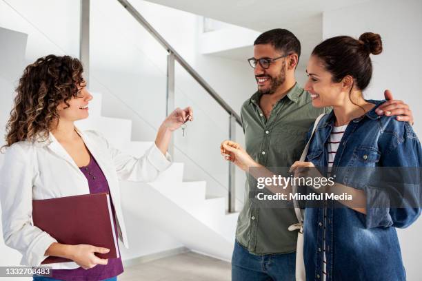 young latin couple receiving keys from real estate agent - contrato de arrendamento imagens e fotografias de stock