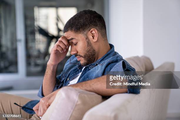vista lateral de un hombre adulto medio sosteniendo su cabeza contra su mano mientras está sentado en casa - infertilidad fotografías e imágenes de stock