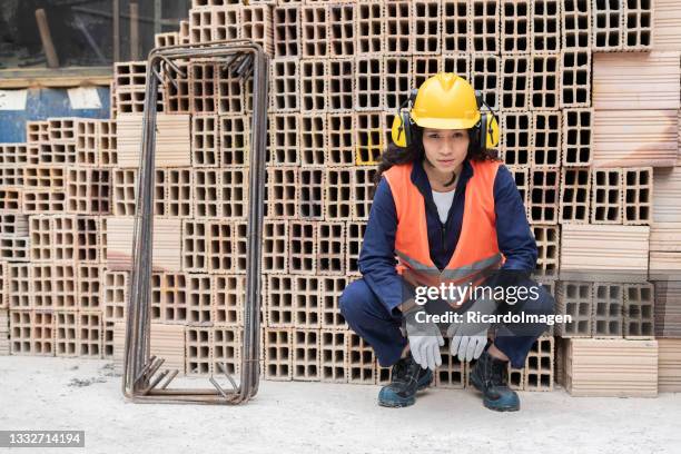25-year-old latin woman construction worker stands in front of a brick tower looking at the camera - dedication brick stock pictures, royalty-free photos & images
