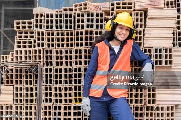 25-year-old latin woman construction worker stands in front of a brick tower looking at the camera - dedication brick stock pictures, royalty-free photos & images