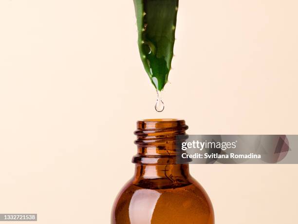 aloe vera leaf with drop falling in glass cosmetic bottle - aloe plant stockfoto's en -beelden