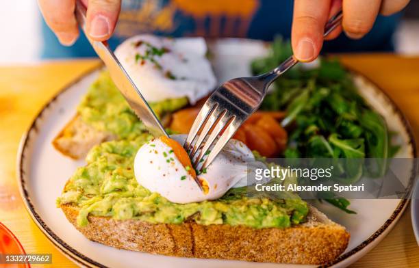 man eating avocado toast with poached egg and salmon, close-up view - cutting avocado stockfoto's en -beelden