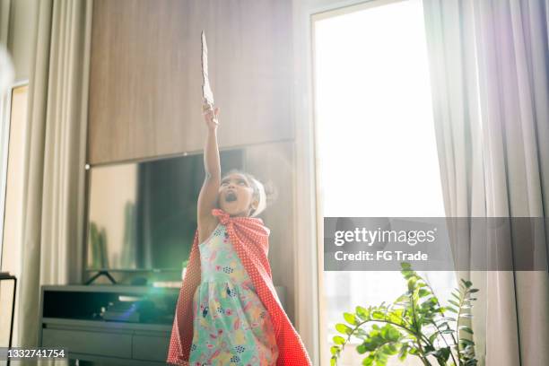 cute girl is playing with a sword and a crown on her head at home - zwarte mantel stockfoto's en -beelden