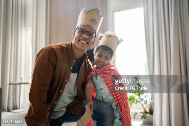portrait of father and daughter playing wearing crown at home - zwarte mantel stockfoto's en -beelden