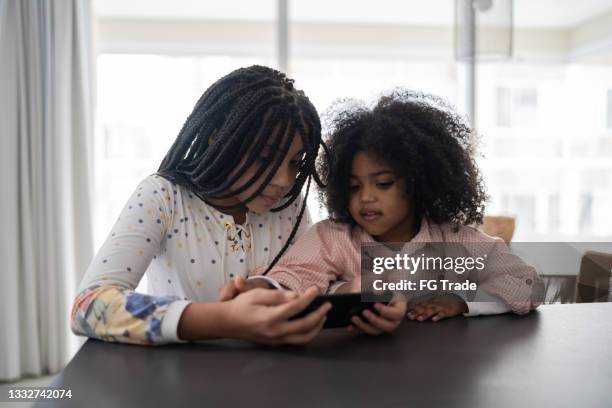 sisters watching something on smartphone at home - modern family media call stockfoto's en -beelden