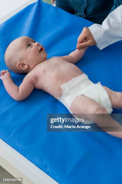 petit garçon de 4 à 6 mois, mentant sur la table d’examen sans chemise regardant le médecin pendant qu’ils le vérifient - table dexamen médical photos et images de collection