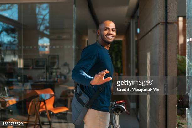 young man arriving by bicycle at the workplace - zwaaien gebaren stockfoto's en -beelden