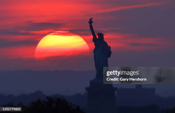 The sun sets behind the Statue of Liberty on August 6, 2021 in New York City.