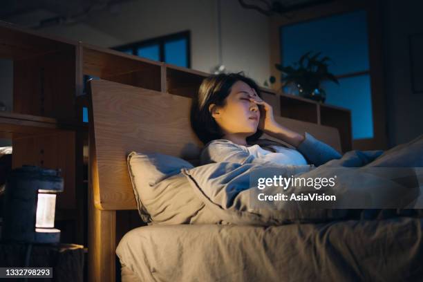 young asian woman feeling sick and suffering from a headache, lying on bed and taking a rest at home - woman cough stock pictures, royalty-free photos & images