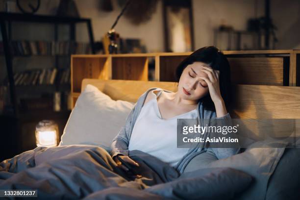 young asian woman feeling sick and suffering from a headache, lying on the bed and taking a rest at home - anemia bildbanksfoton och bilder