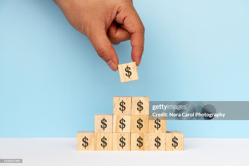 Hands Stacking Dollar Signs on Wood Toy Block