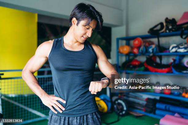 joven deportista musculoso hombre comprobando los datos sobre el rastreador de fitness después de entrenar en el gimnasio. concepto de salud y fitness. - handsome bodybuilders fotografías e imágenes de stock