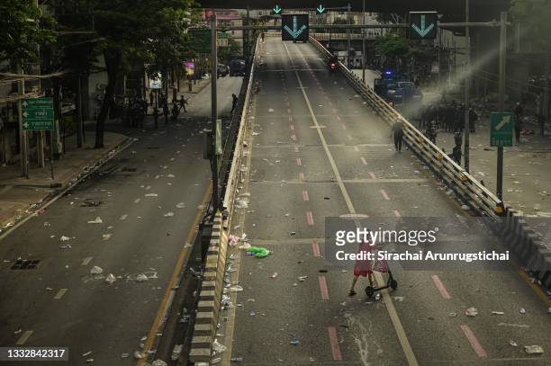 Woman crosses a street strewn with debris after a confrontation between anti-government protesters and riot police on August 07, 2021 in Bangkok,...