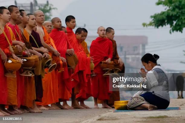 woman offering alms to monks in "tak bat" ritual - vang vieng stock pictures, royalty-free photos & images