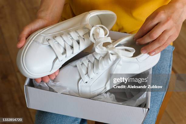 the girl takes out new clean white modern sneakers from the package. a woman or a teenager unpacks sports shoes from a box, at home or indoors. ordering and delivery of clothes and things at home. stay at home. a fashionable and stylish lifestyle. - white shoe stock pictures, royalty-free photos & images