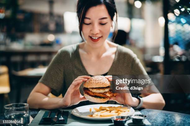 smiling young asian woman enjoying freshly made delicious burger with fries in a restaurant - fat asian woman 個照片及圖片檔