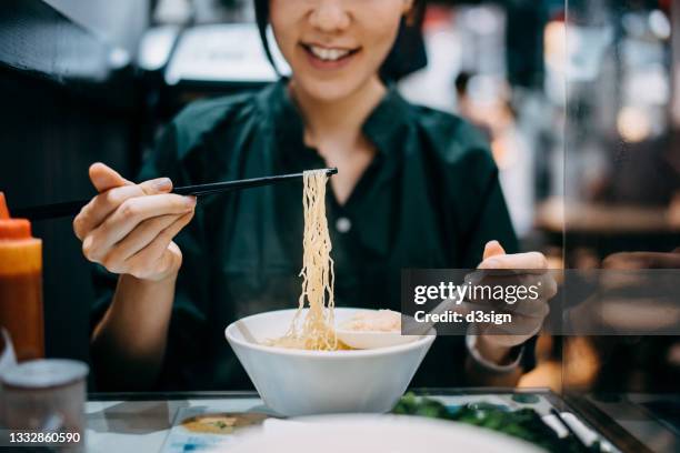 close up of smiling young asian woman eating freshly served hong kong style wonton soup noodle with chopsticks in a local restaurant. traditional local food culture. eating out lifestyle - noodle soup stock pictures, royalty-free photos & images