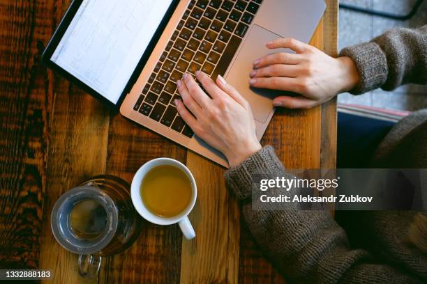 women's hands type text on the keyboard of a computer or laptop, in a cafe or coworking space. an office worker at his desk. the concept of business, freelancing, working at home. next to it is a teapot with herbal green tea, a glass. take a break. - wahlregistrierungskarte stock-fotos und bilder