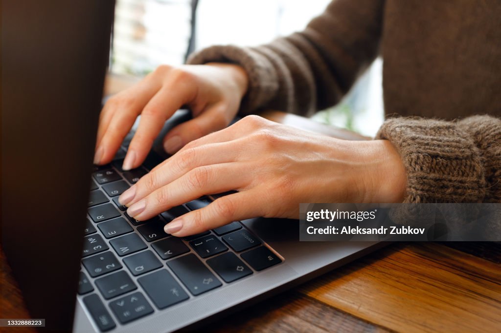 Women's hands type text on the keyboard of a computer or laptop, in a cafe or coworking space. An office worker at his desk. The concept of business, freelancing, working at home. Close-up.