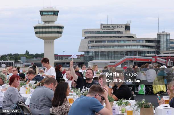 People, including a man with a paper airplane, attend the "Freedom Dinner" on the runway at former Tegel Airport on August 07, 2021 in Berlin,...