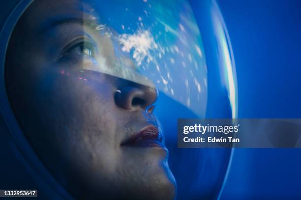 asian chinese mid adult female astronaut looking at earth through window from spaceship at outer space - cosmonaut stockfoto's en -beelden