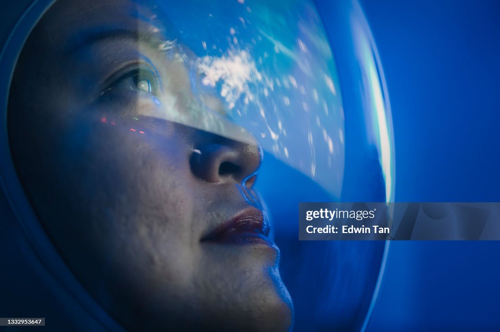 Asian chinese mid adult female astronaut looking at earth through window from spaceship at outer space