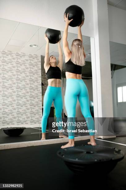 back view of a young caucasian woman exercising in front of the mirror in the gym using a medicine ball. - medicine ball stock pictures, royalty-free photos & images