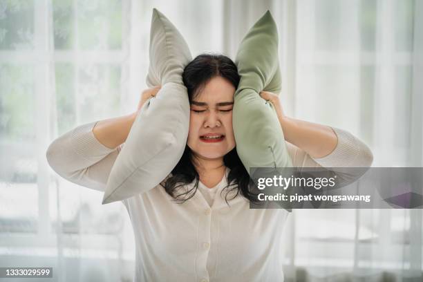 fat woman covering her ears with a pillow, the concept does not want to hear things. affecting oneself - chubby face stockfoto's en -beelden