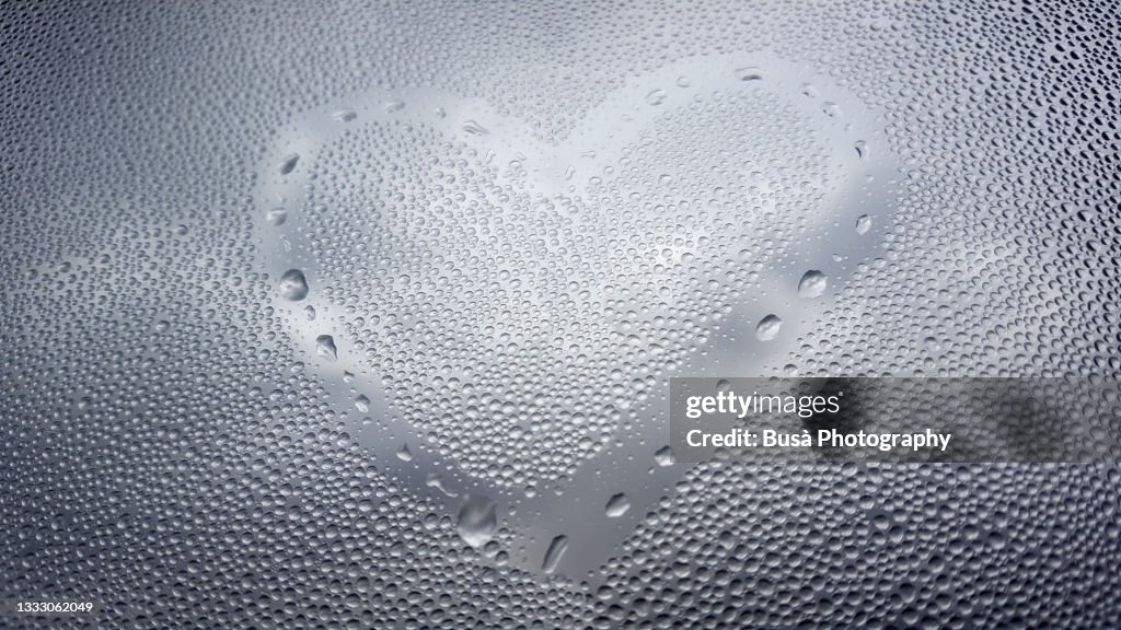 Drawing of a heart shape on dew droplets on window glass