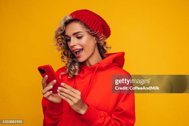 schöne frau, die vor blauem hintergrund mit smartphone steht - red shirt stock-fotos und bilder