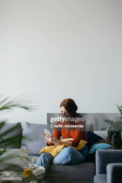 mujer alegre usando el teléfono móvil en casa - people on sofa fotografías e imágenes de stock