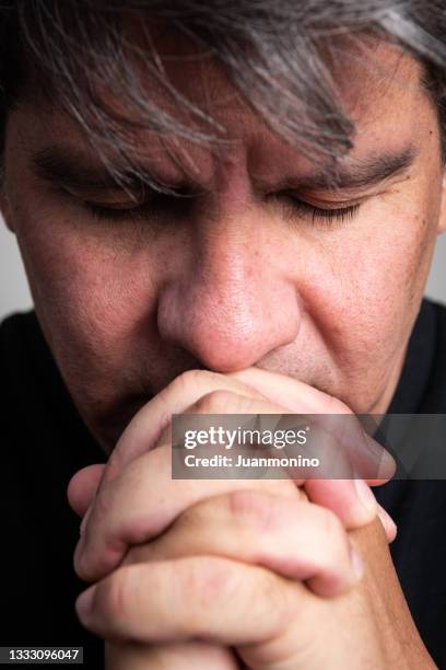 pensive mature man praying looking down with his hands together - grief hands stock pictures, royalty-free photos & images