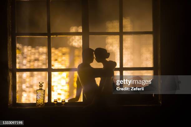 A realistic dollhouse living room with furniture and window at night. Romantic couple sitting on window. Artwork table decoration with handmade realistic dollhouse. Selective focus.