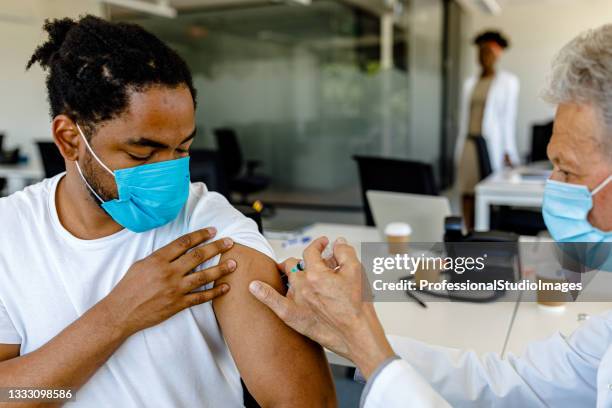 vaccination of a young african man at the doctor's office. - afghan old man stock pictures, royalty-free photos & images