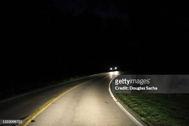 approaching headlights on a spooky rural road - nähern stock-fotos und bilder
