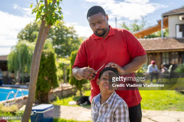 un padre premuroso che dà al figlio un taglio di capelli a casa - jamaican ethnicity foto e immagini stock