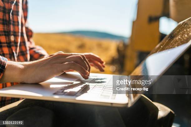 nahaufnahme der hände von bäuerinnen mit laptop neben mähdreschermaschine - place stock-fotos und bilder